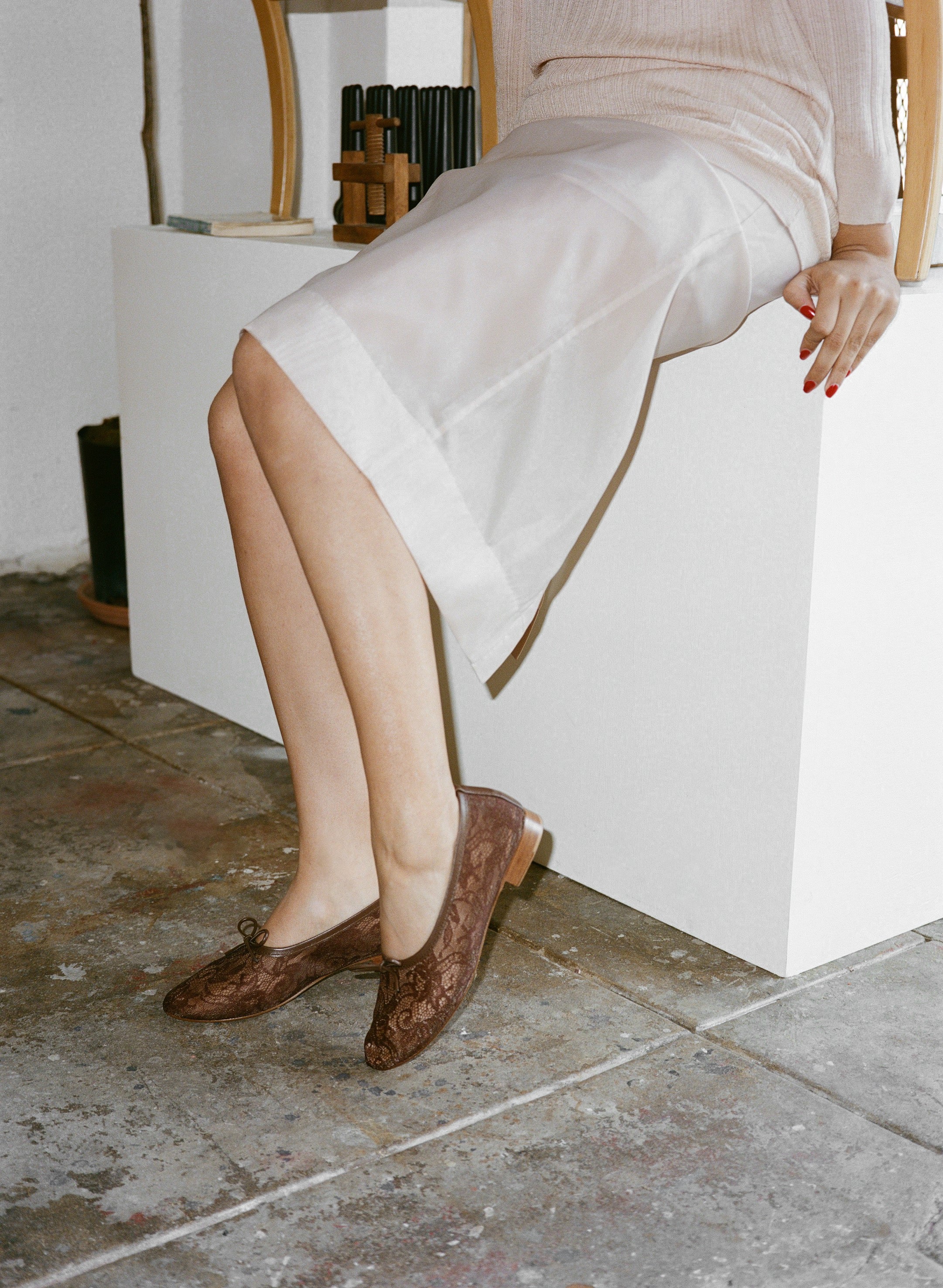 Person wearing a white skirt and brown lace shoes sitting on a white block.