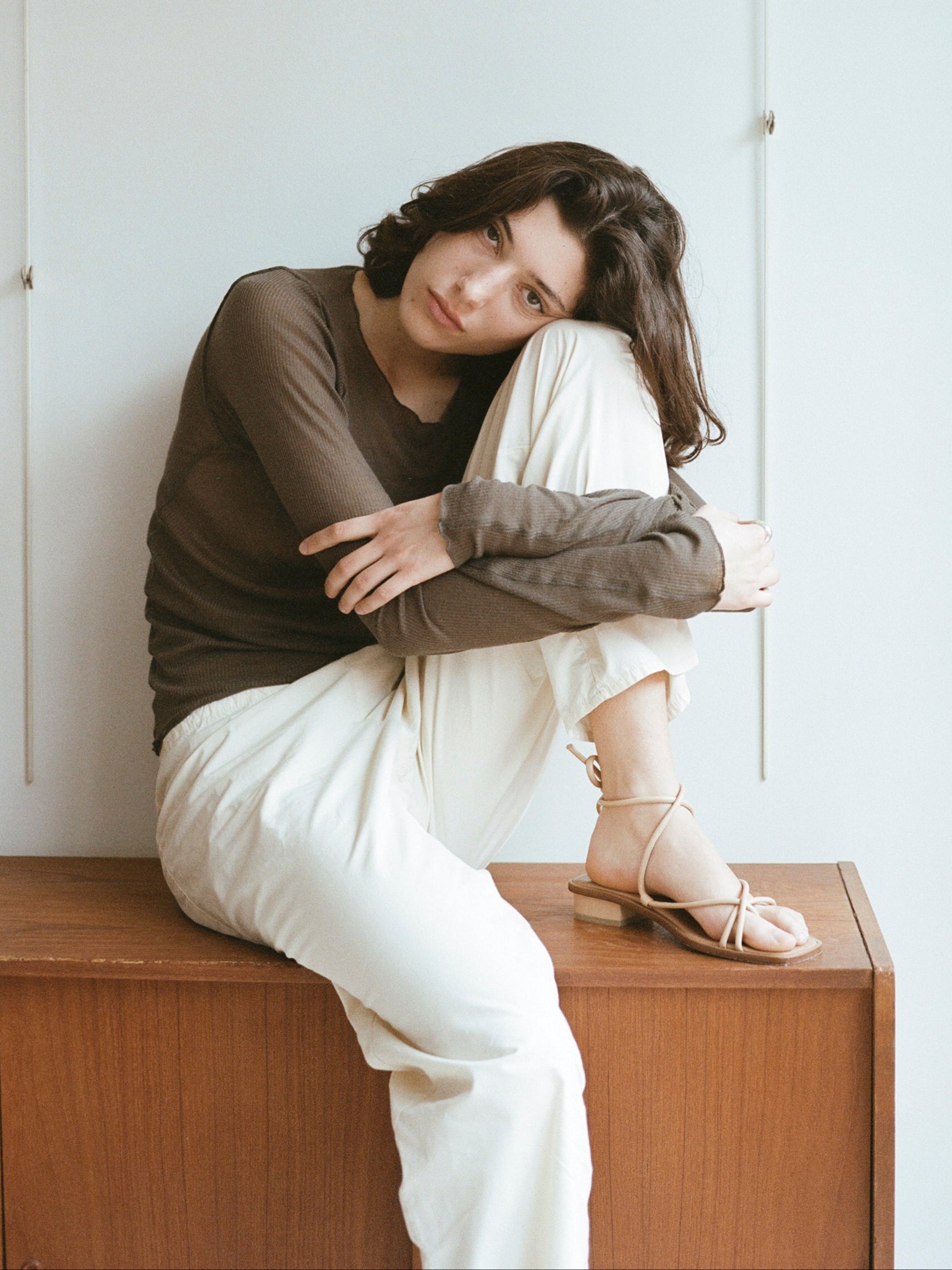 Model wears light beige sandals with tubular straps that cross the top of the feet and wrap around the ankles to tie.