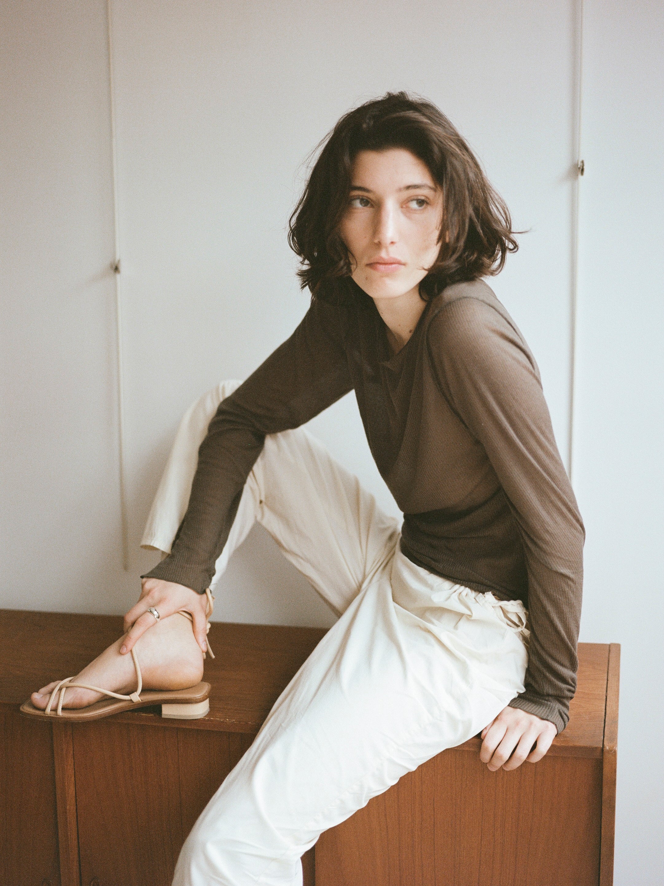 Model wears light beige sandals with tubular straps that cross the top of the feet and wrap around the ankles to tie.