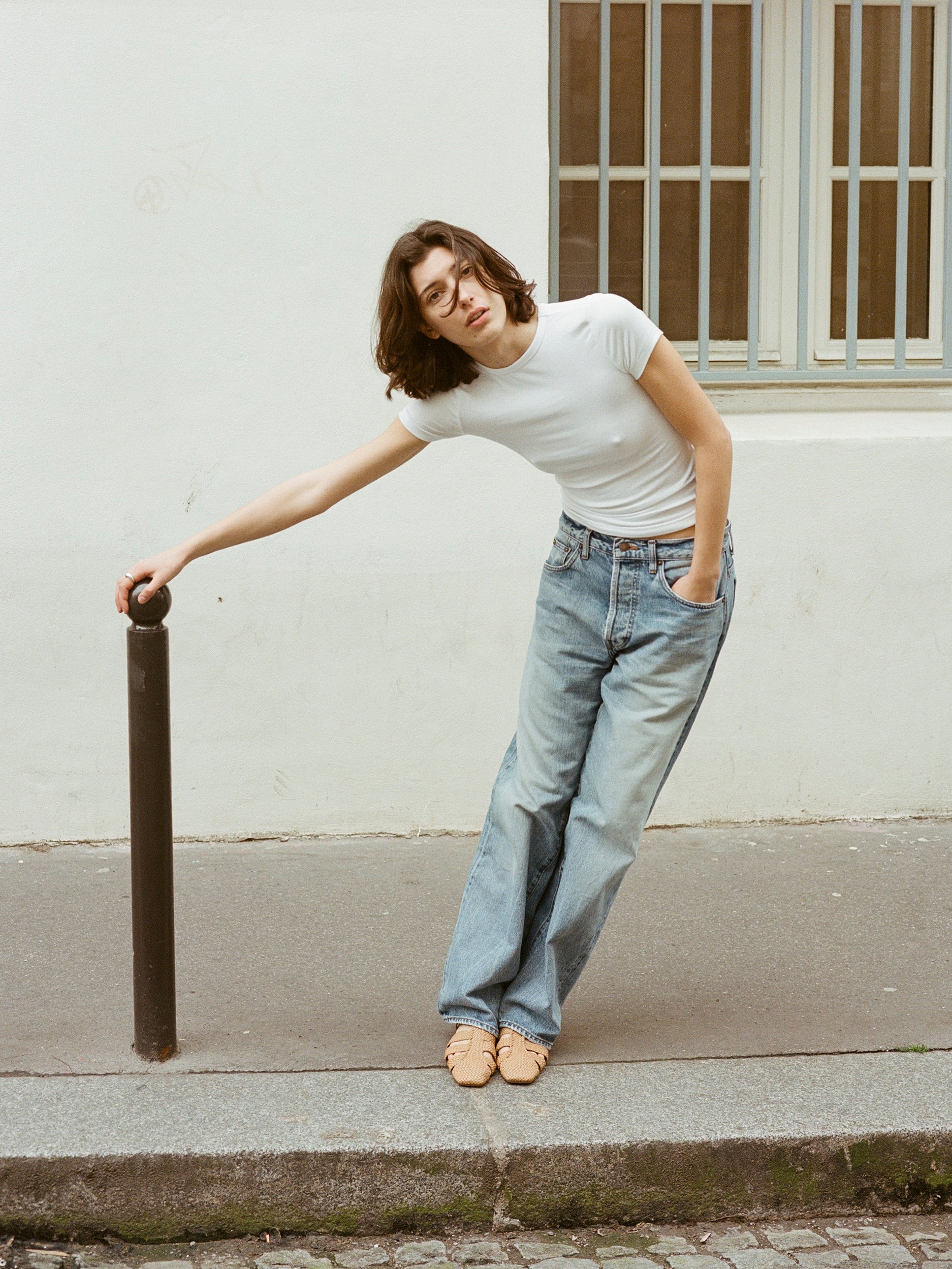 Model wears tan leather fisherman-style sandals featuring straps made of woven leather across the foot and a strap that buckles around the ankle