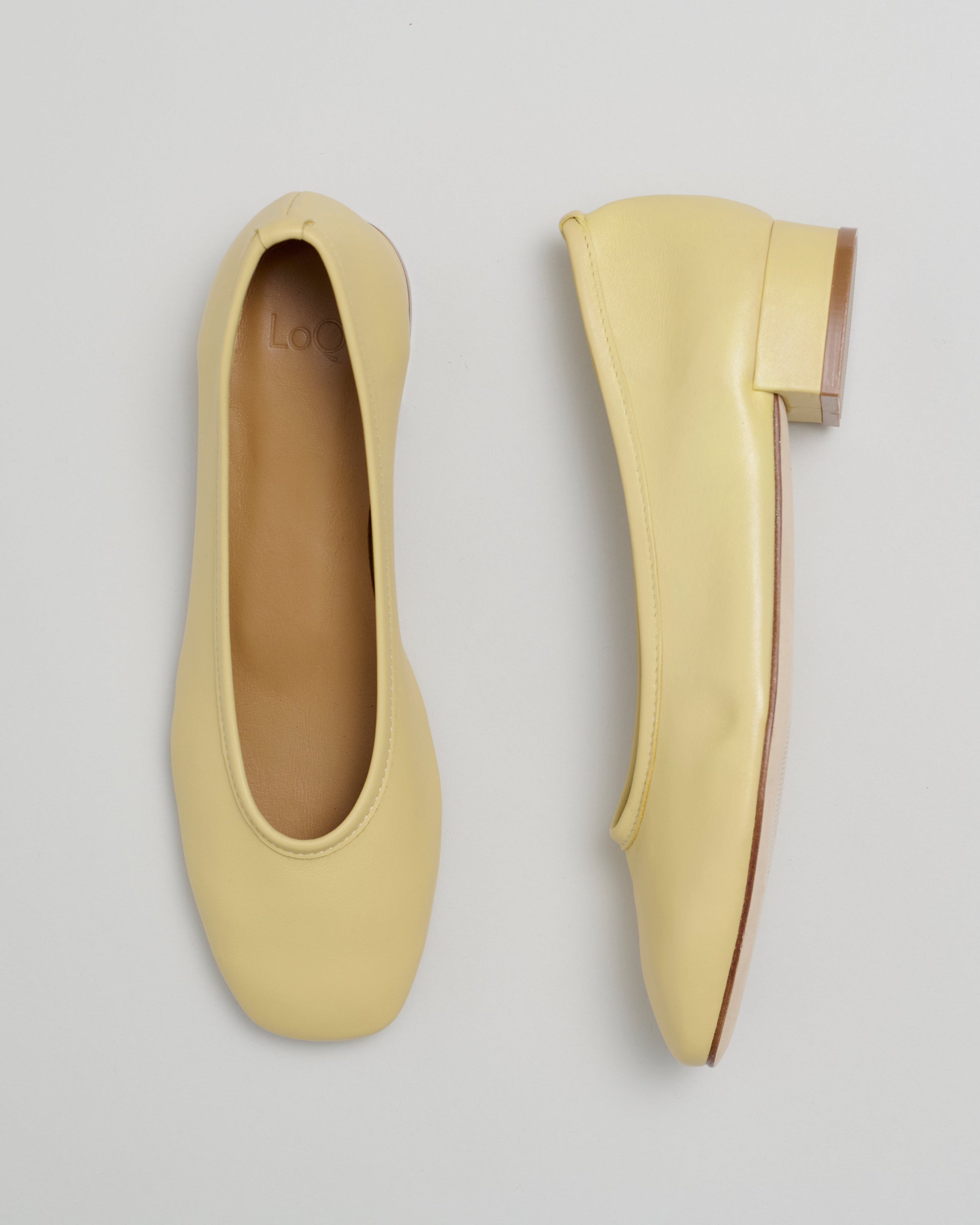 Pair of light yellow, low-heel pumps on a gray background