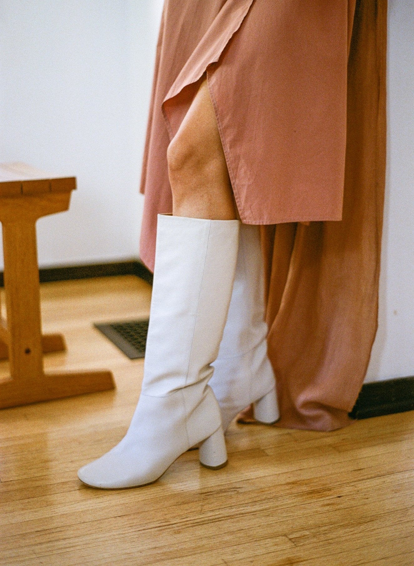 Model wears tall pull-on boot in a supple cream, off-white leather that sits below the knee with a round toe.