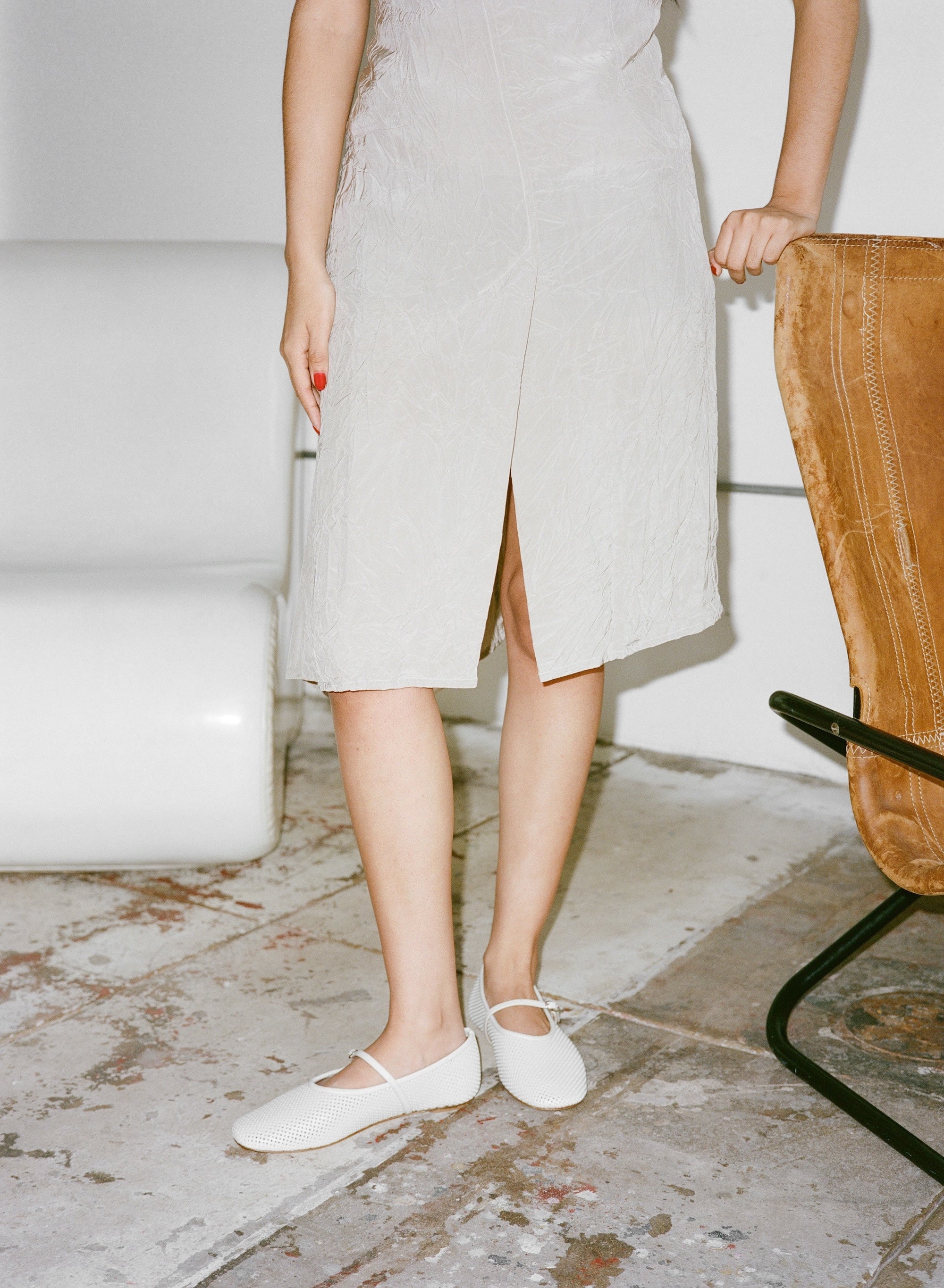Person wearing a light-colored dress and white shoes on a textured floor.