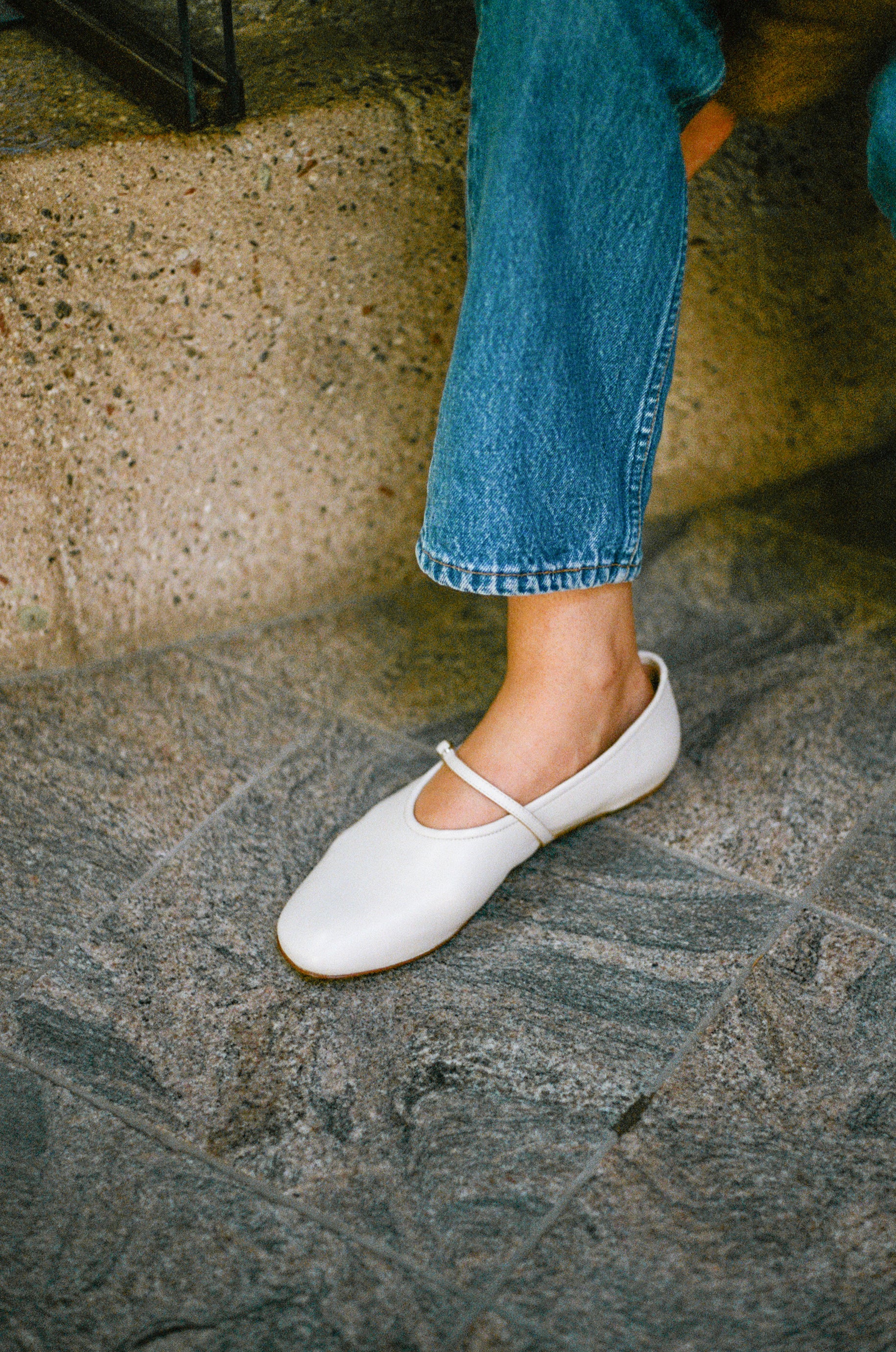 Model wears off white colored leather mary jane style flat shoe with strap and buckle closure.