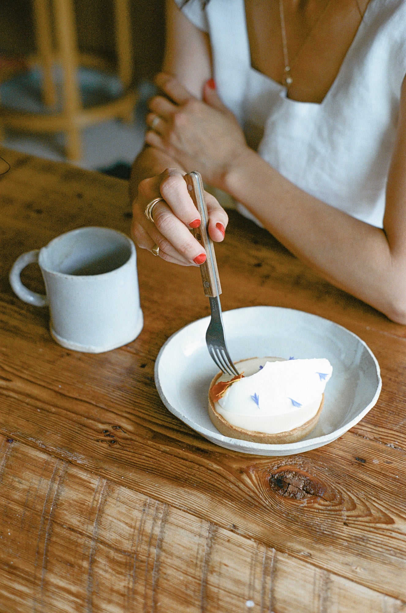Model poses with white ceramic mug and plate with pastry.