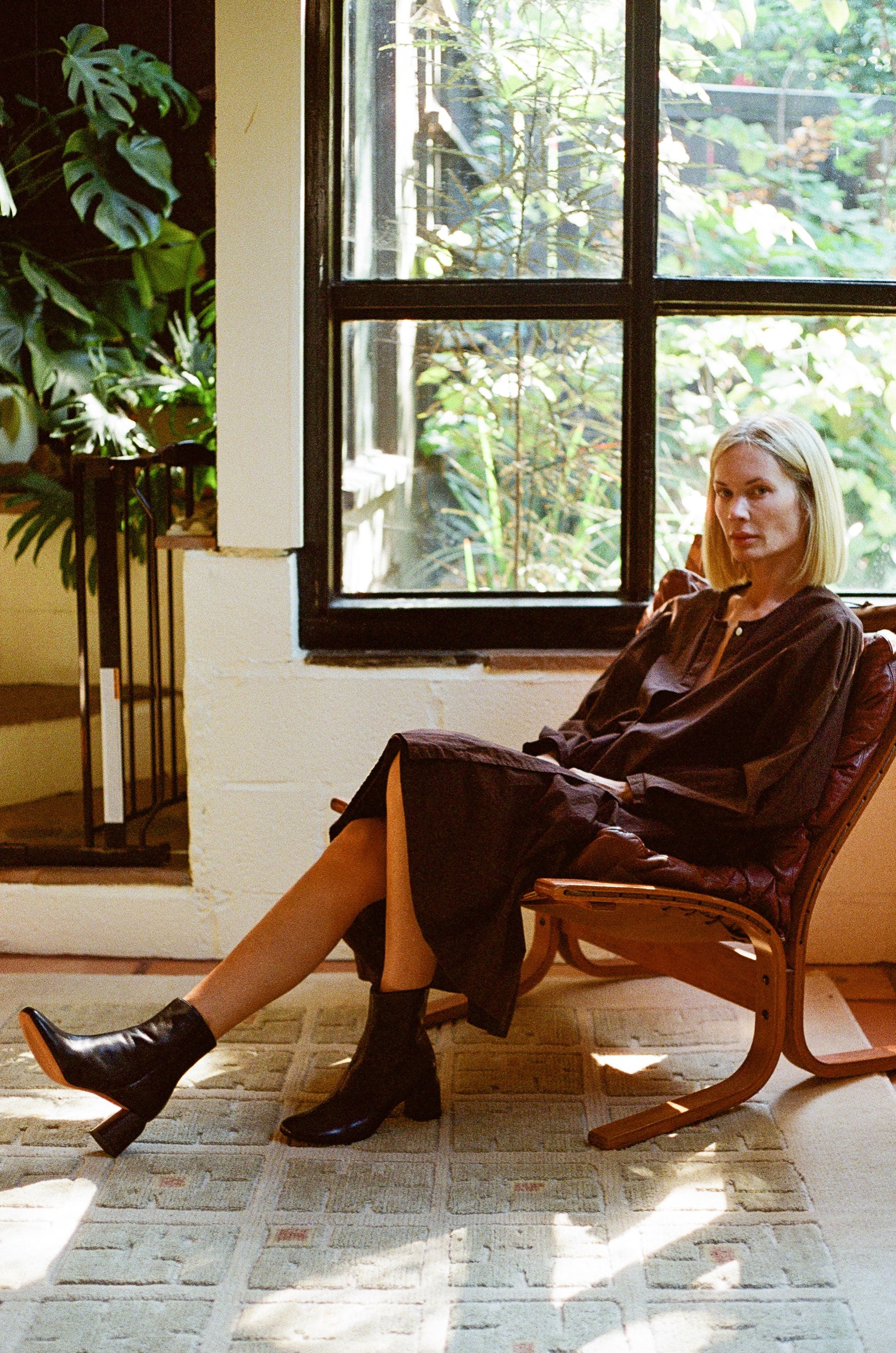 Woman sitting in a chair by a window with plants in the background