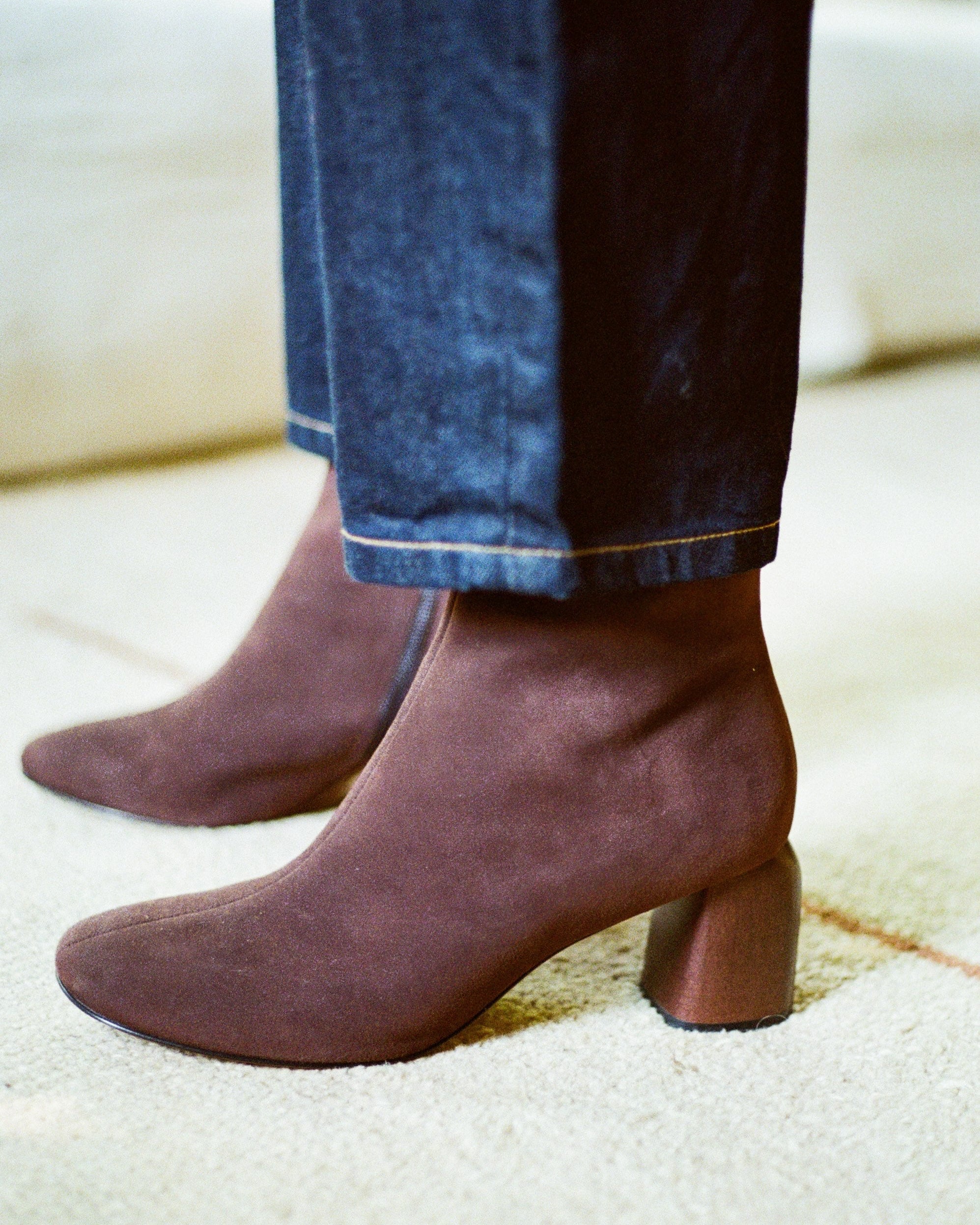 Brown suede boots worn with blue jeans on a light-colored floor.