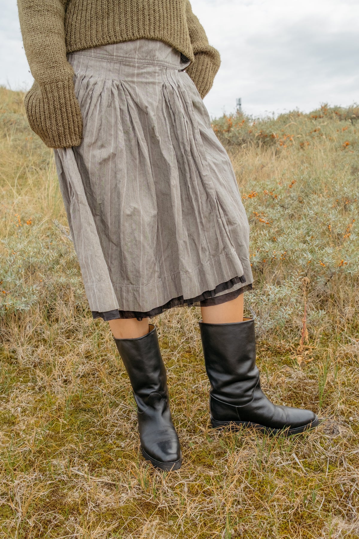 A person standing outdoors in a grassy field wearing black mid calf-high boots.
