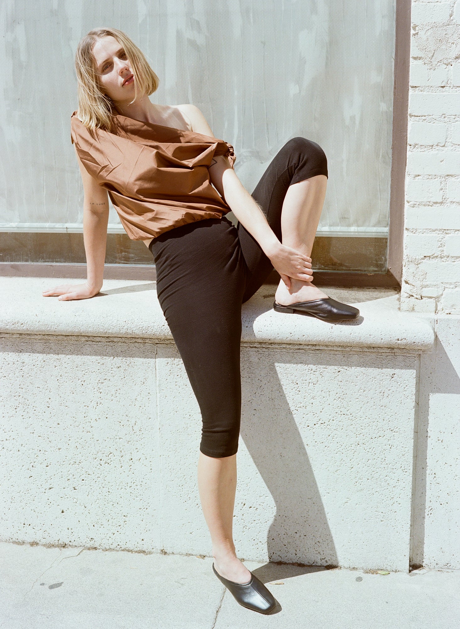 Model wears flat black leather slides with v shaped upper and center seam.