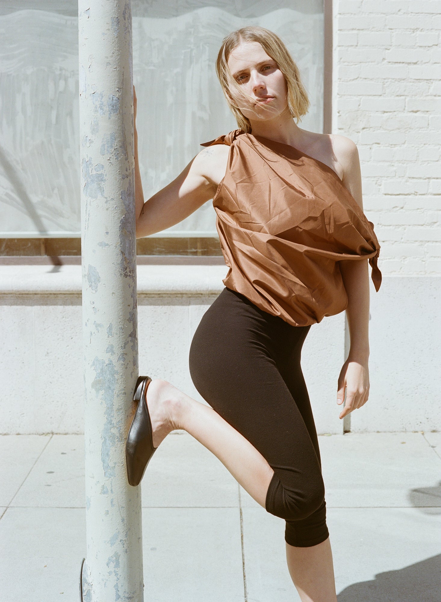 Model wears flat black leather slides with v shaped upper and center seam.