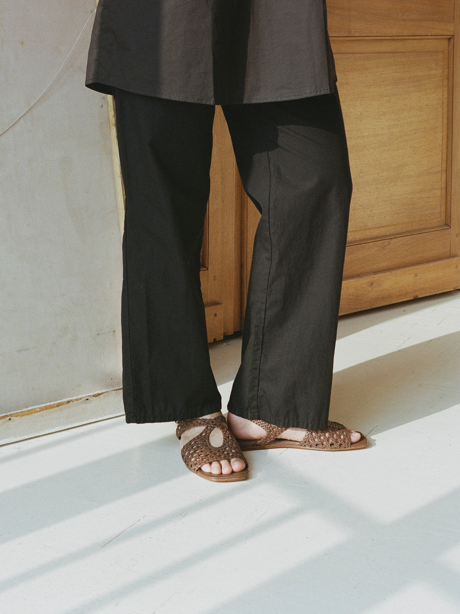 Model wears brown slingback sandals with braided upper and silver buckle clasp.