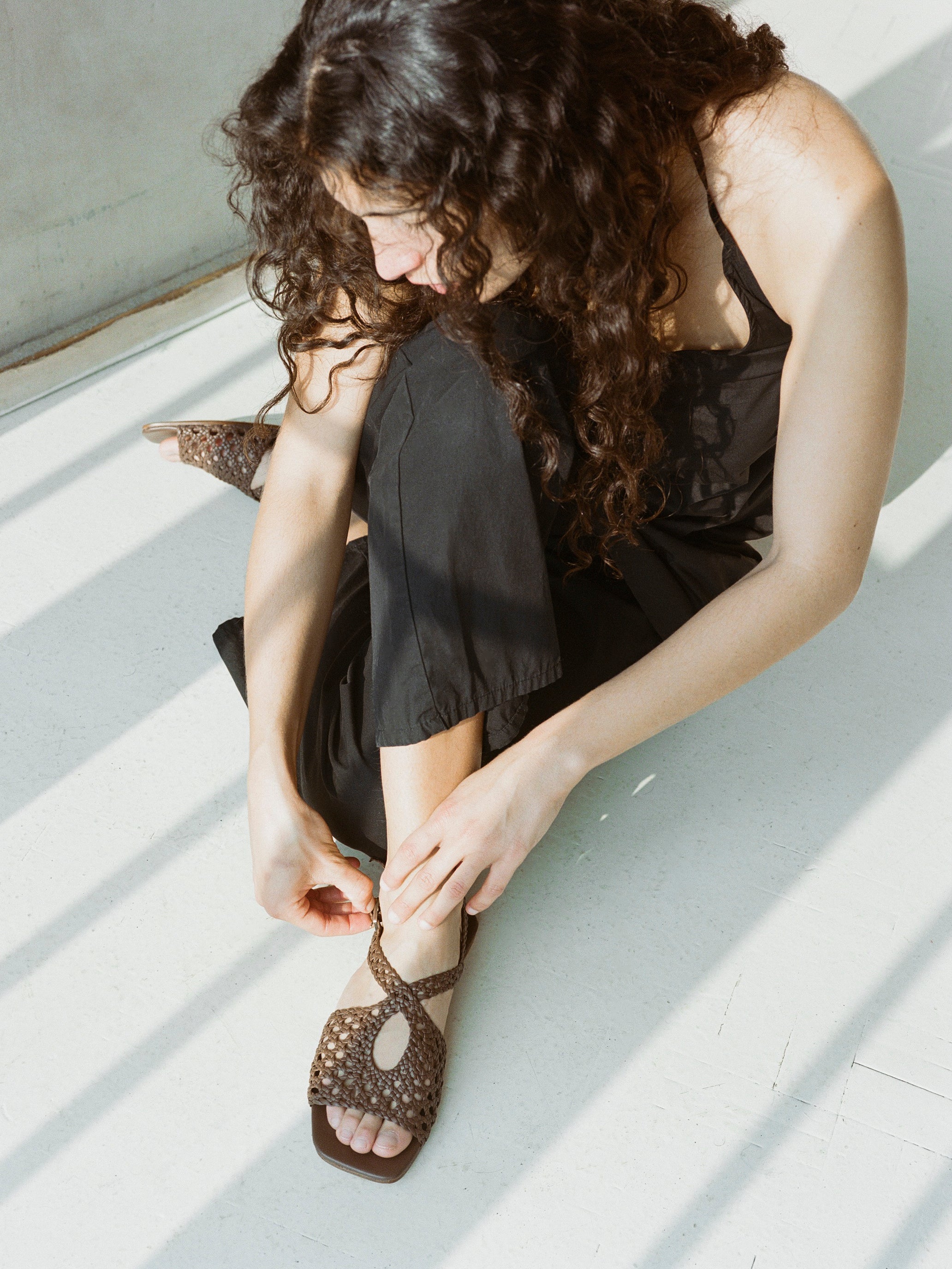 Model wears brown slingback sandals with braided upper and silver buckle clasp.