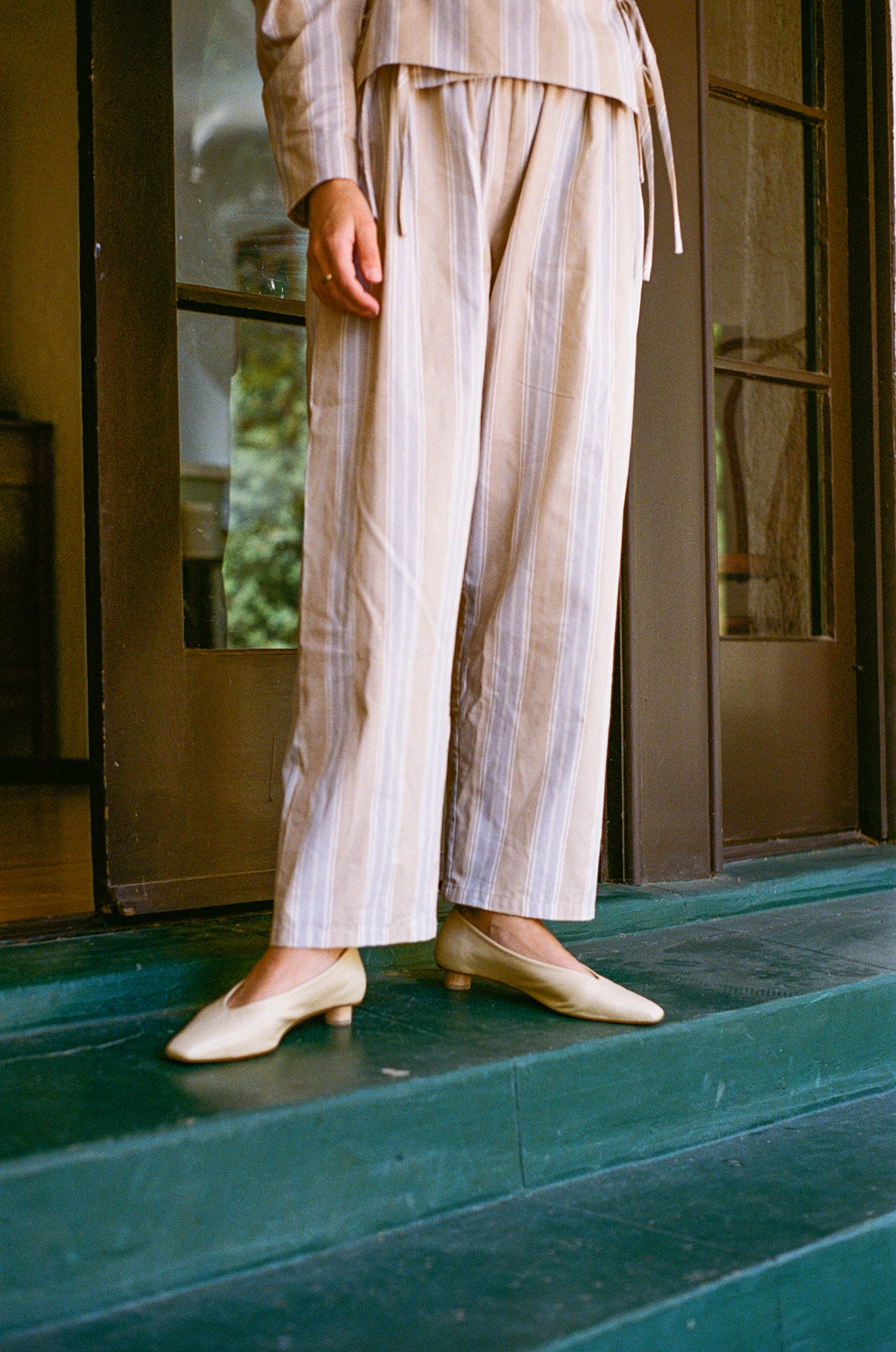 Model wears light tan colored leather ballet flat with short, cylindrical wood heel.
