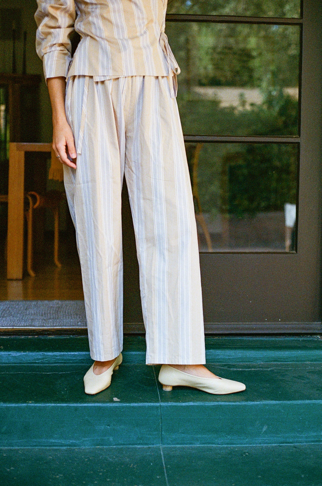 Model wears light tan colored leather ballet flat with short, cylindrical wood heel.