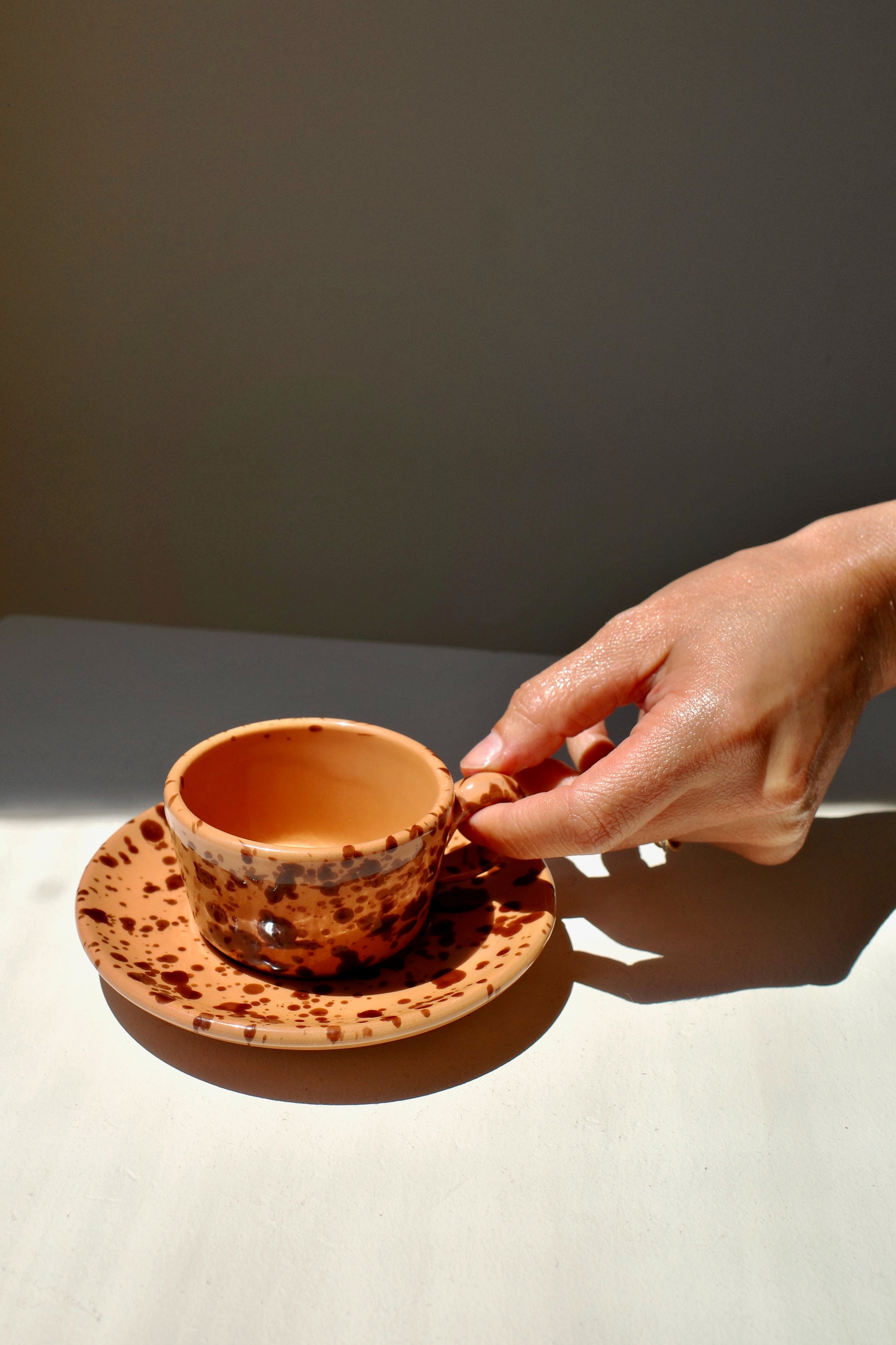 Ceramic espresso cups and saucer with terracotta glaze and dark brown splatter pattern.