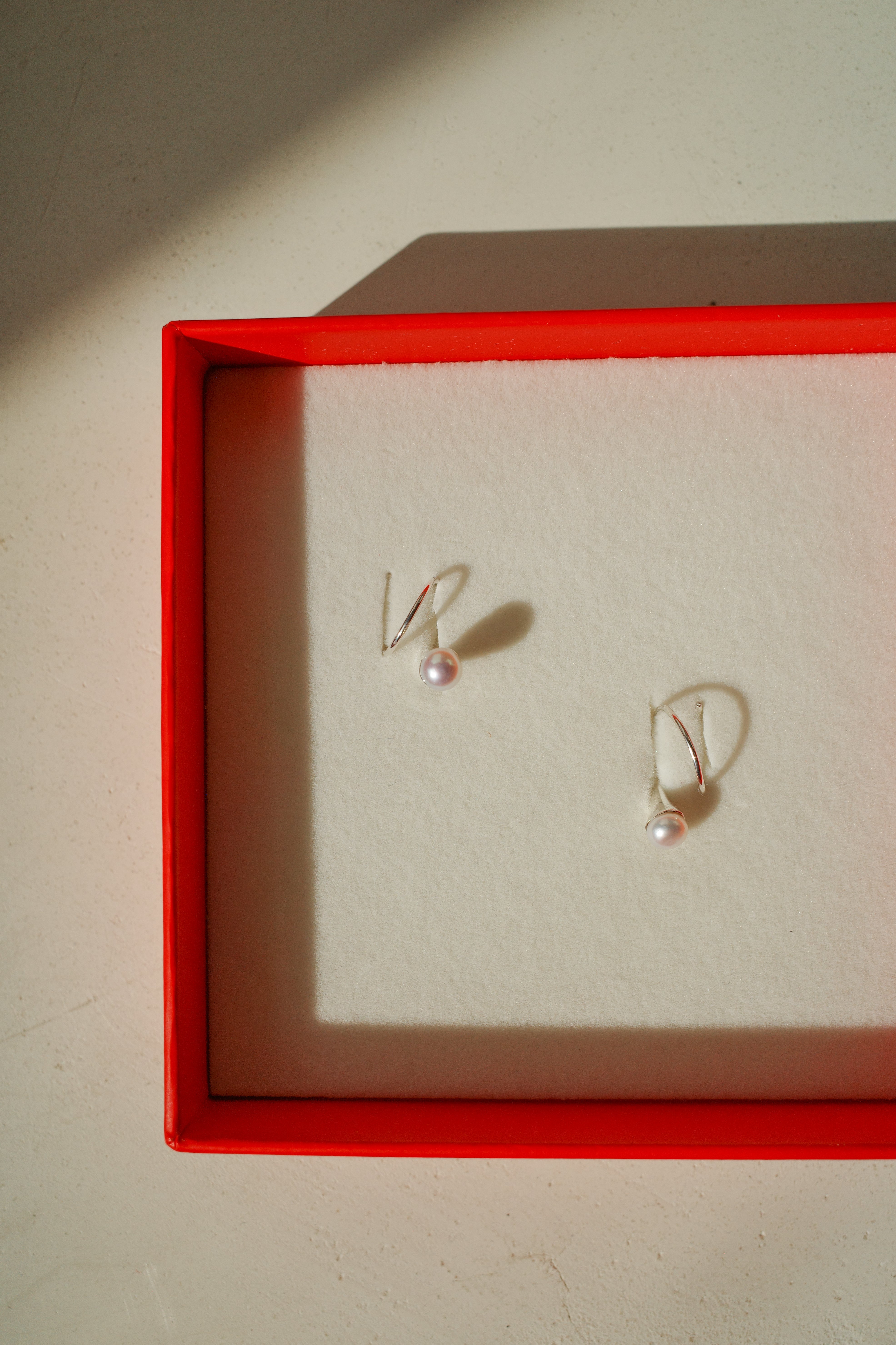Sterling silver earrings that wrap through piercing around lobe with a small pearl adornment in red box.