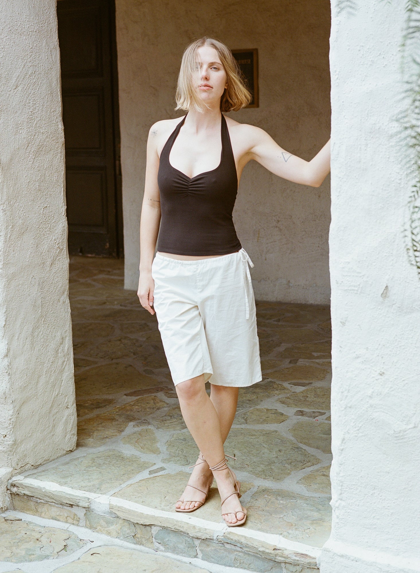 Model wears taupe heeled sandals featuring strappy ankle wrap and tie.
