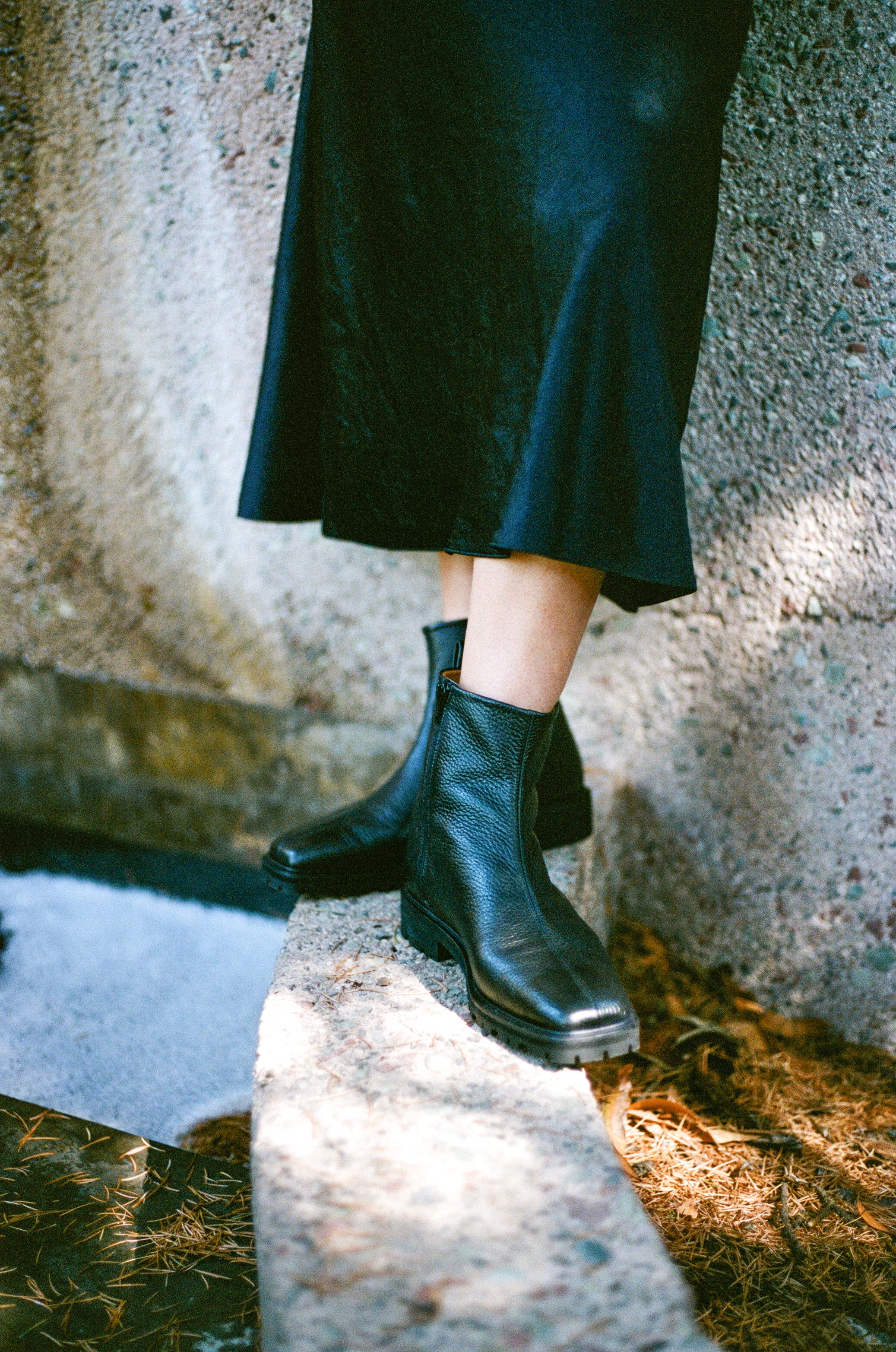 Model wears black tumble leather ankle boot with rubber tread sole and side zipper.