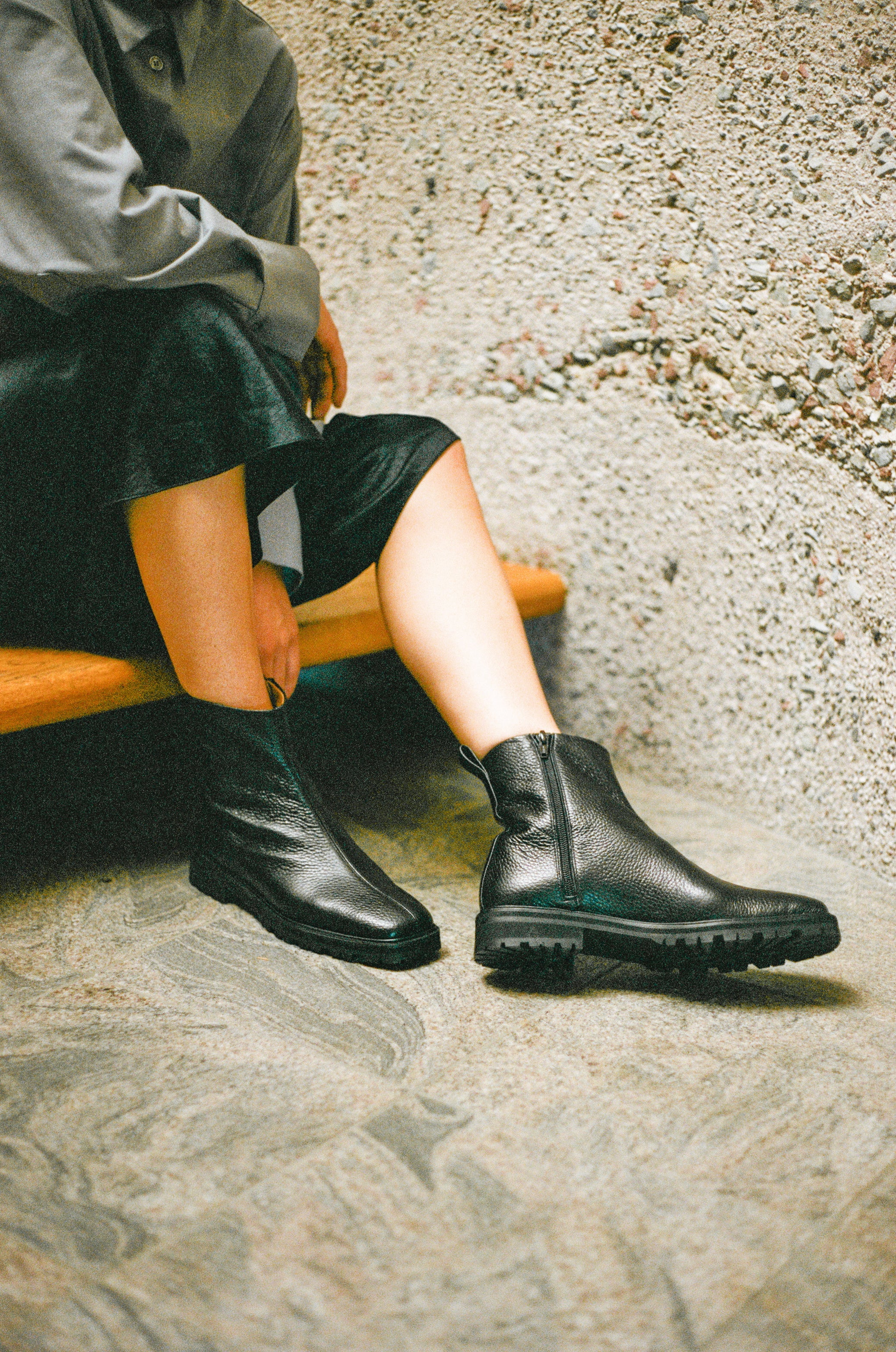 Model wears black tumble leather ankle boot with rubber tread sole and side zipper.