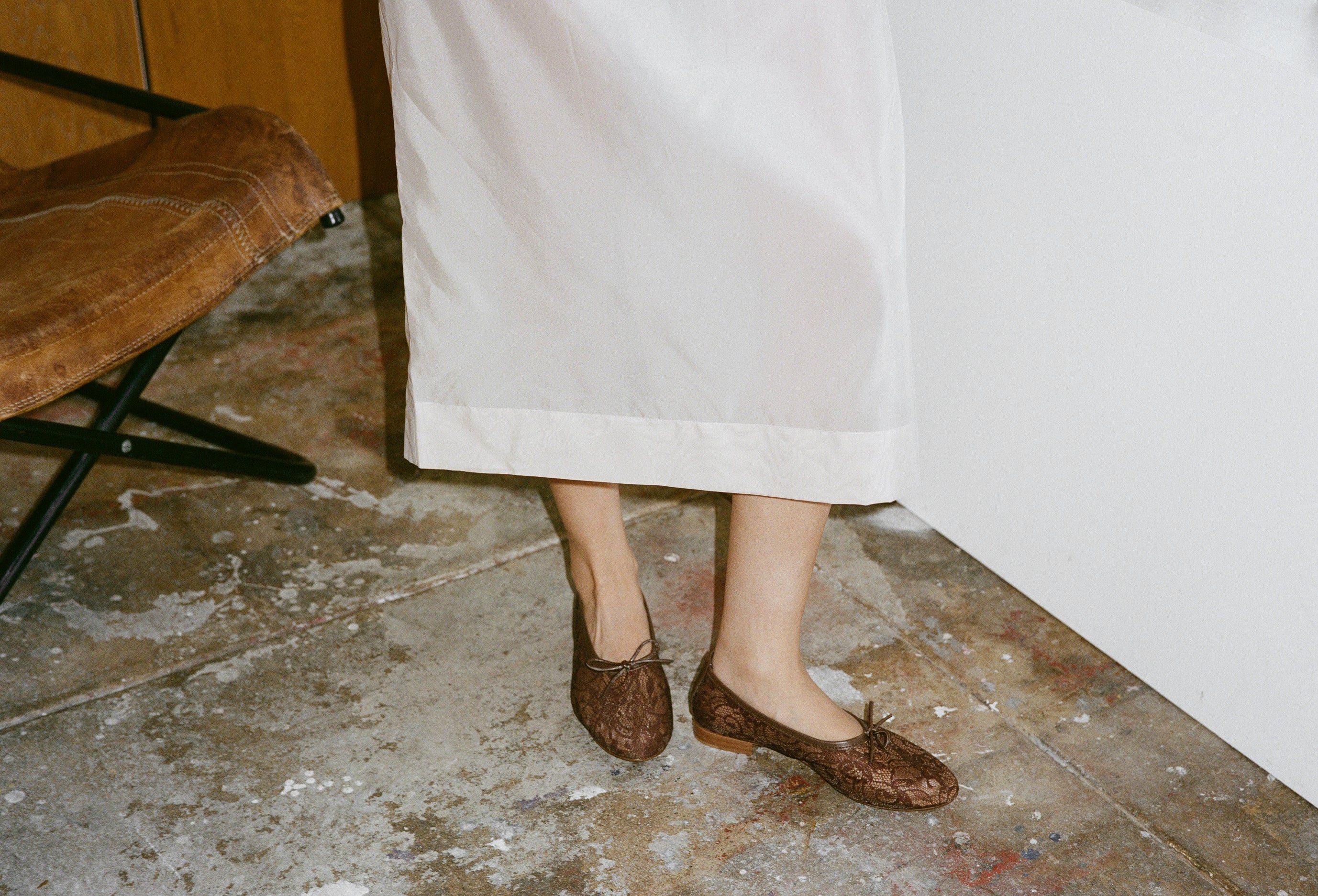 Brown lace shoes worn with a white skirt on a stone floor.