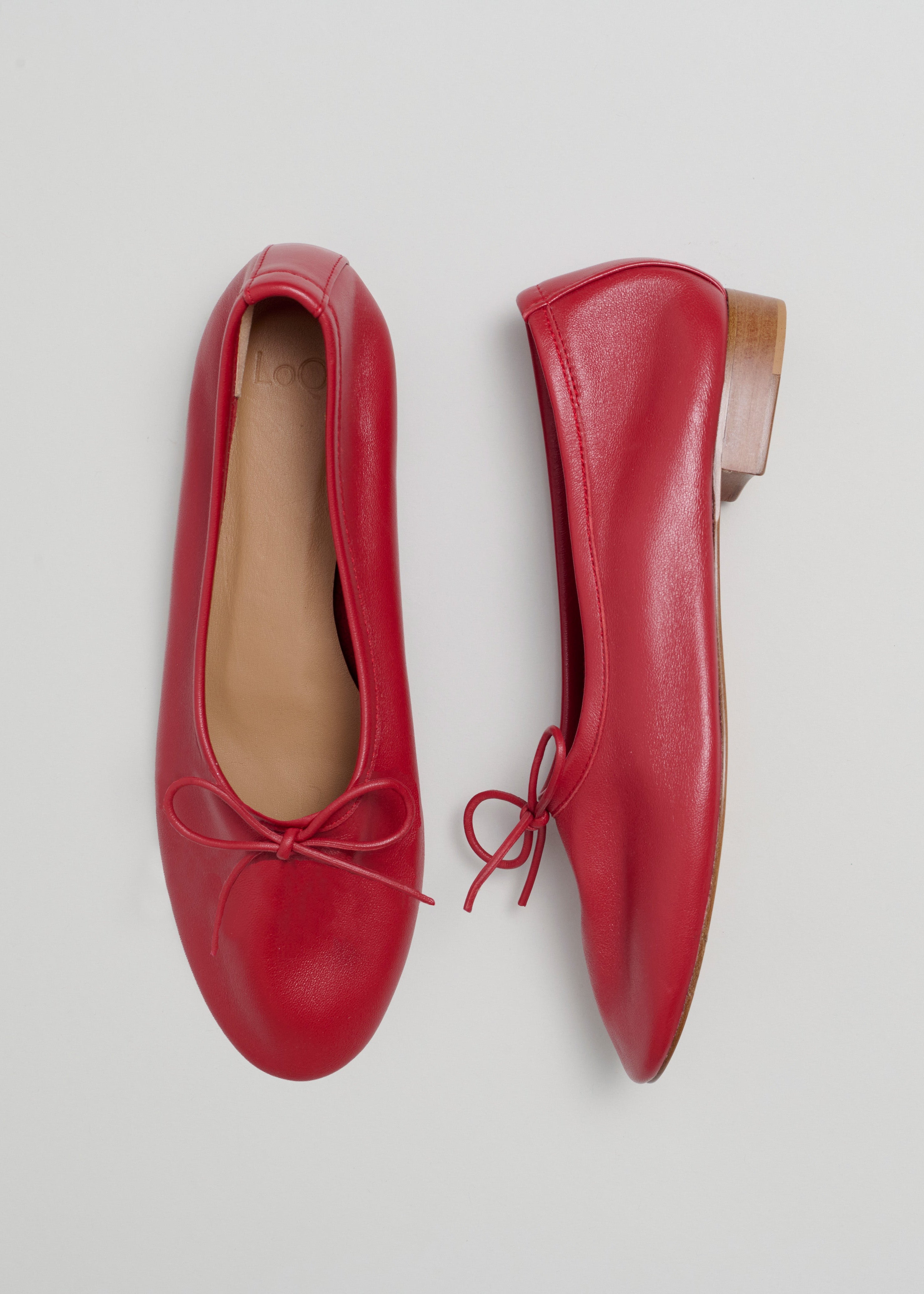 Pair of red leather shoes with a bow on a light gray background