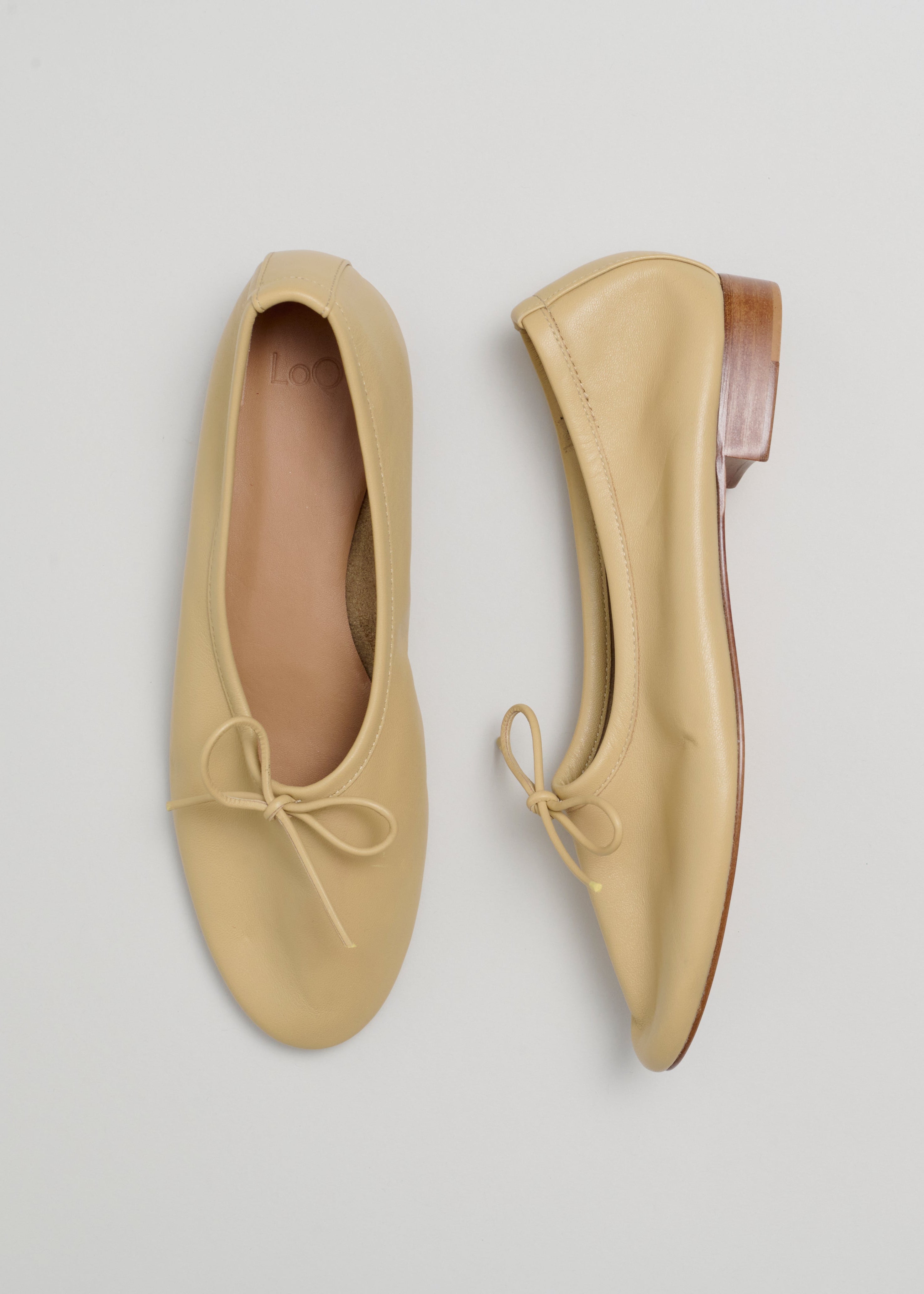 Pair of beige flat shoes with a bow on a light gray background
