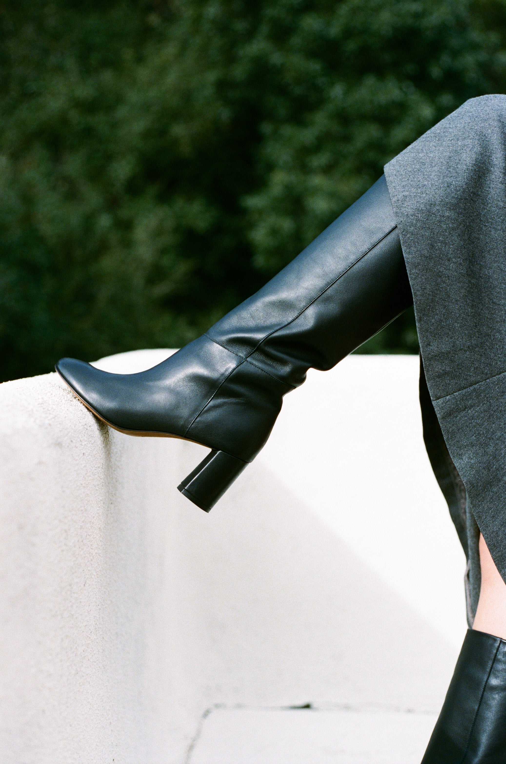 Model wears tall black riding style boot with heel.