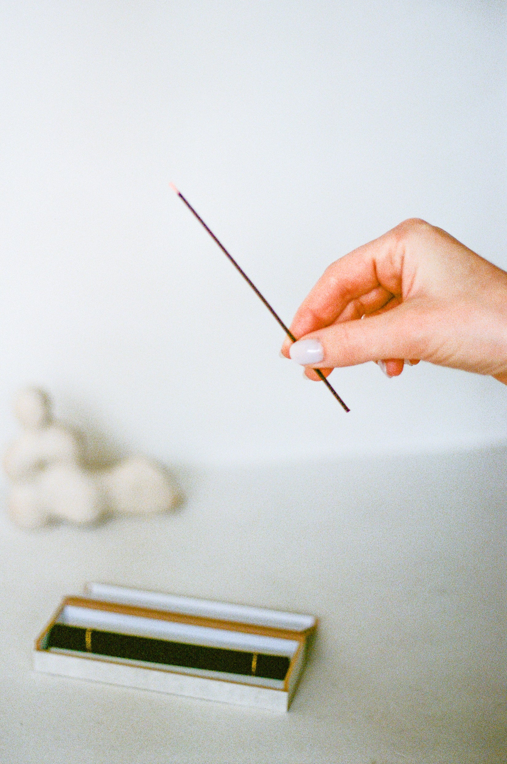 Model holds incense stick above box of incense next to sculpture.