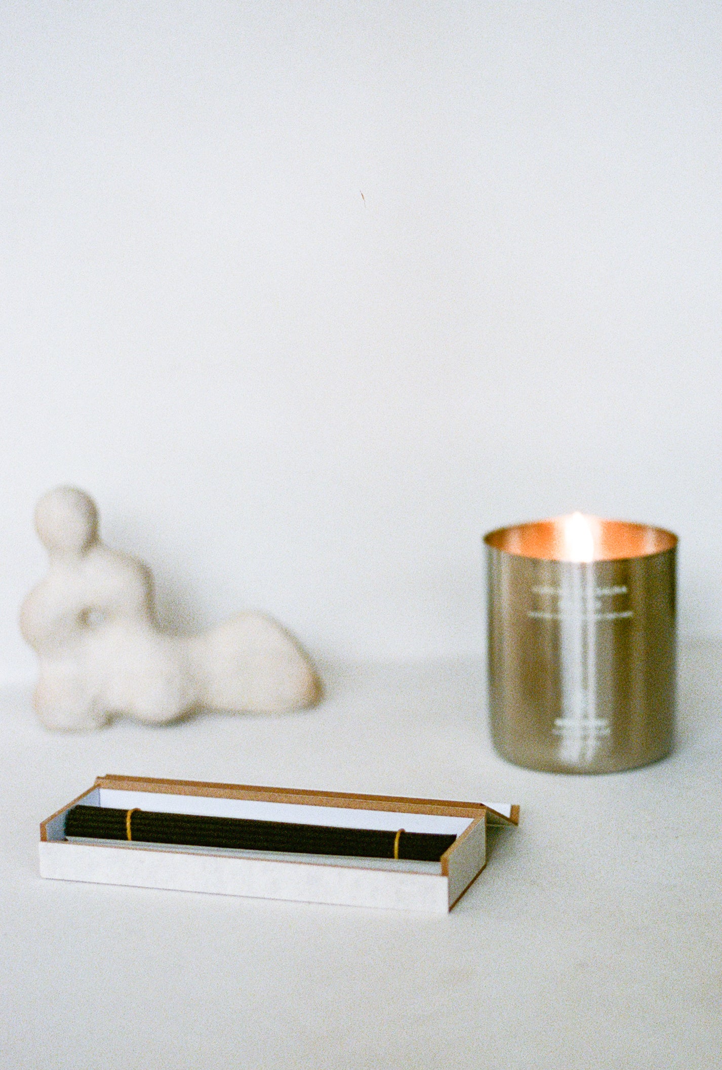 Open box of incense next to candle and sculpture.