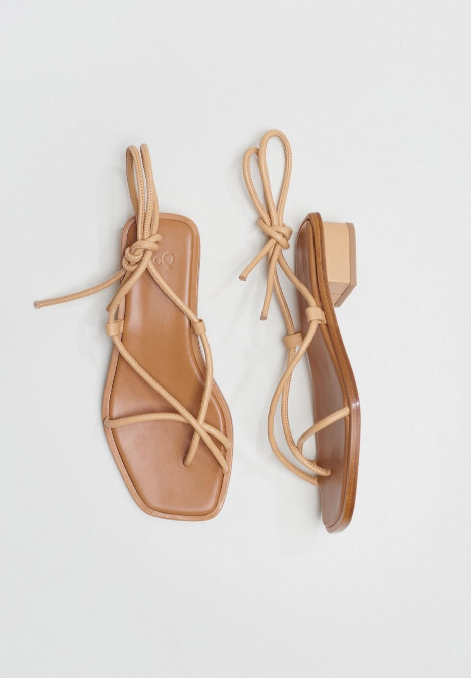 Light beige sandals with tubular straps that cross the top of the feet and wrap around the ankles to tie.