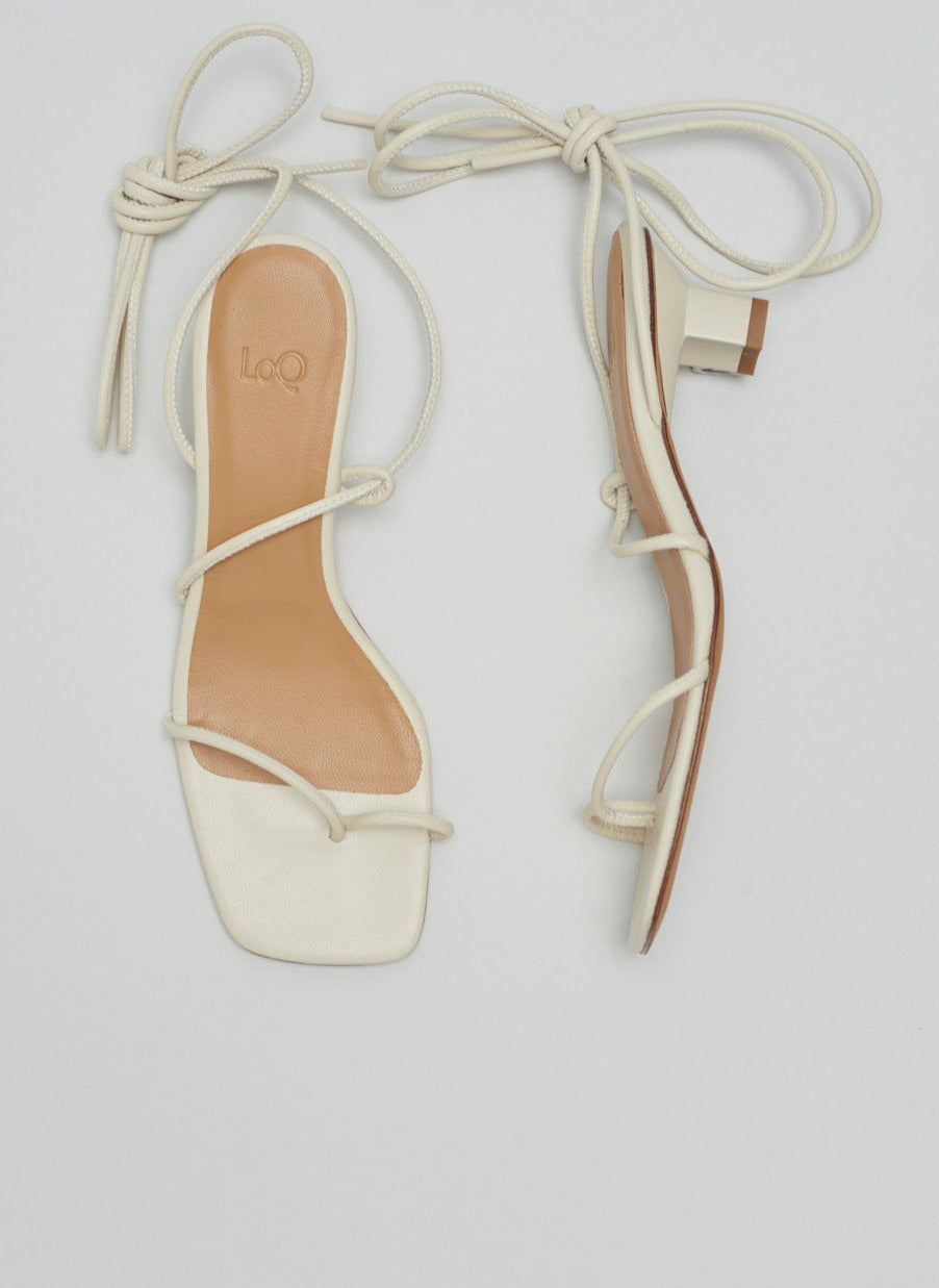 Heeled sandal in off-white leather featuring tubular leather straps that tie at the ankle and a small sculptural 2" heel; a minimal strap divides at the toe.