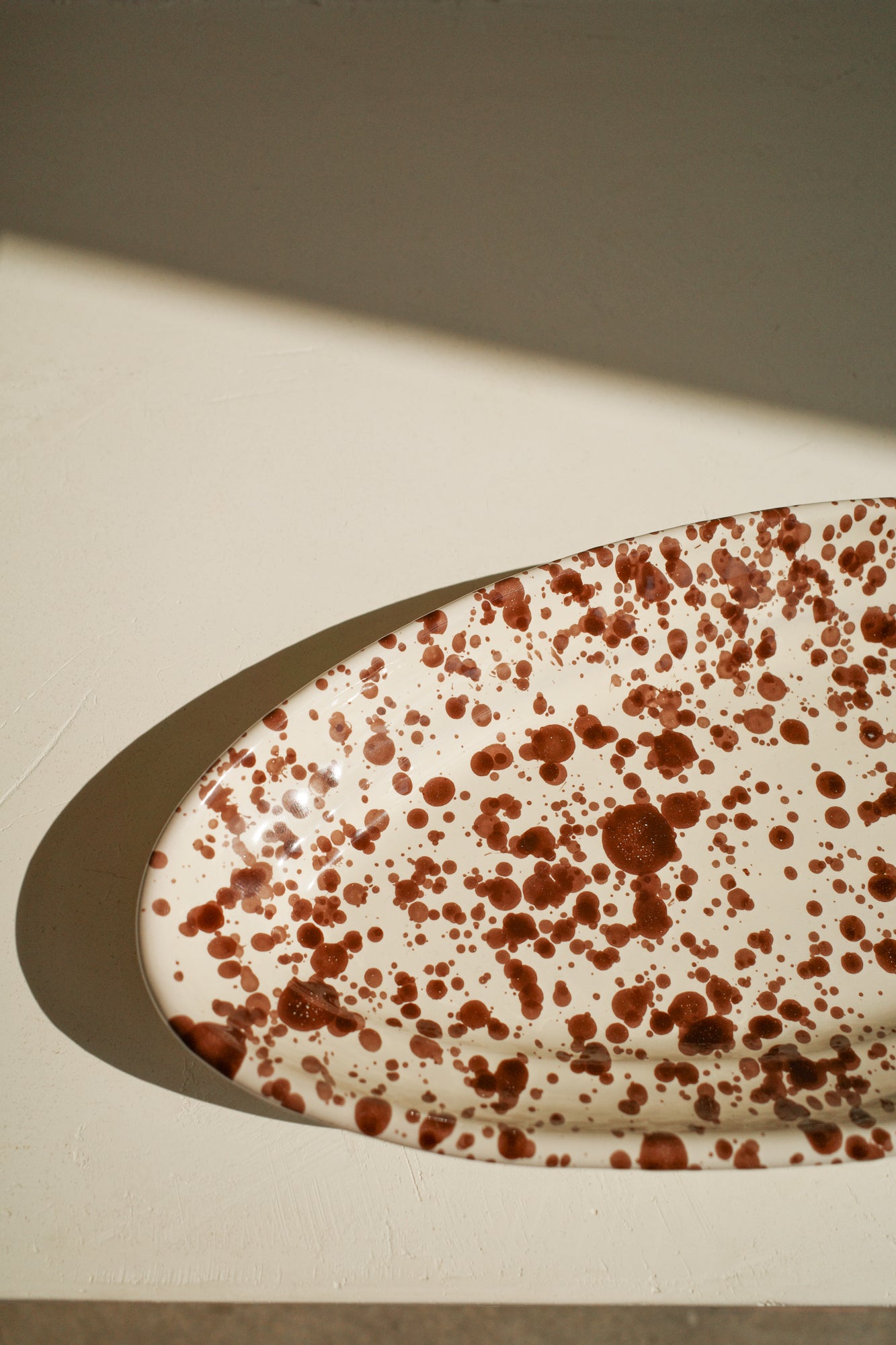 Ceramic oval plate with white glaze and dark brown paint splatter.