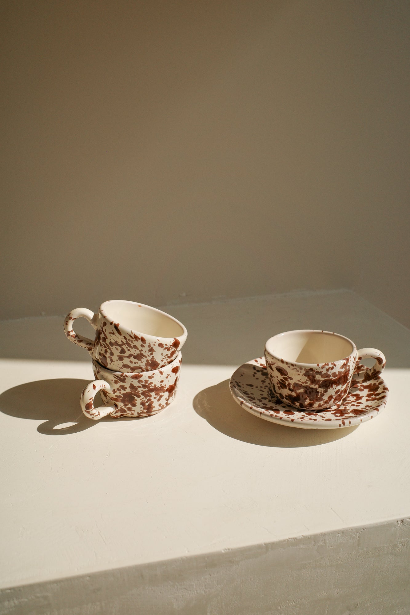 Ceramic espresso cups and saucer with white glaze and dark brown splatter pattern.