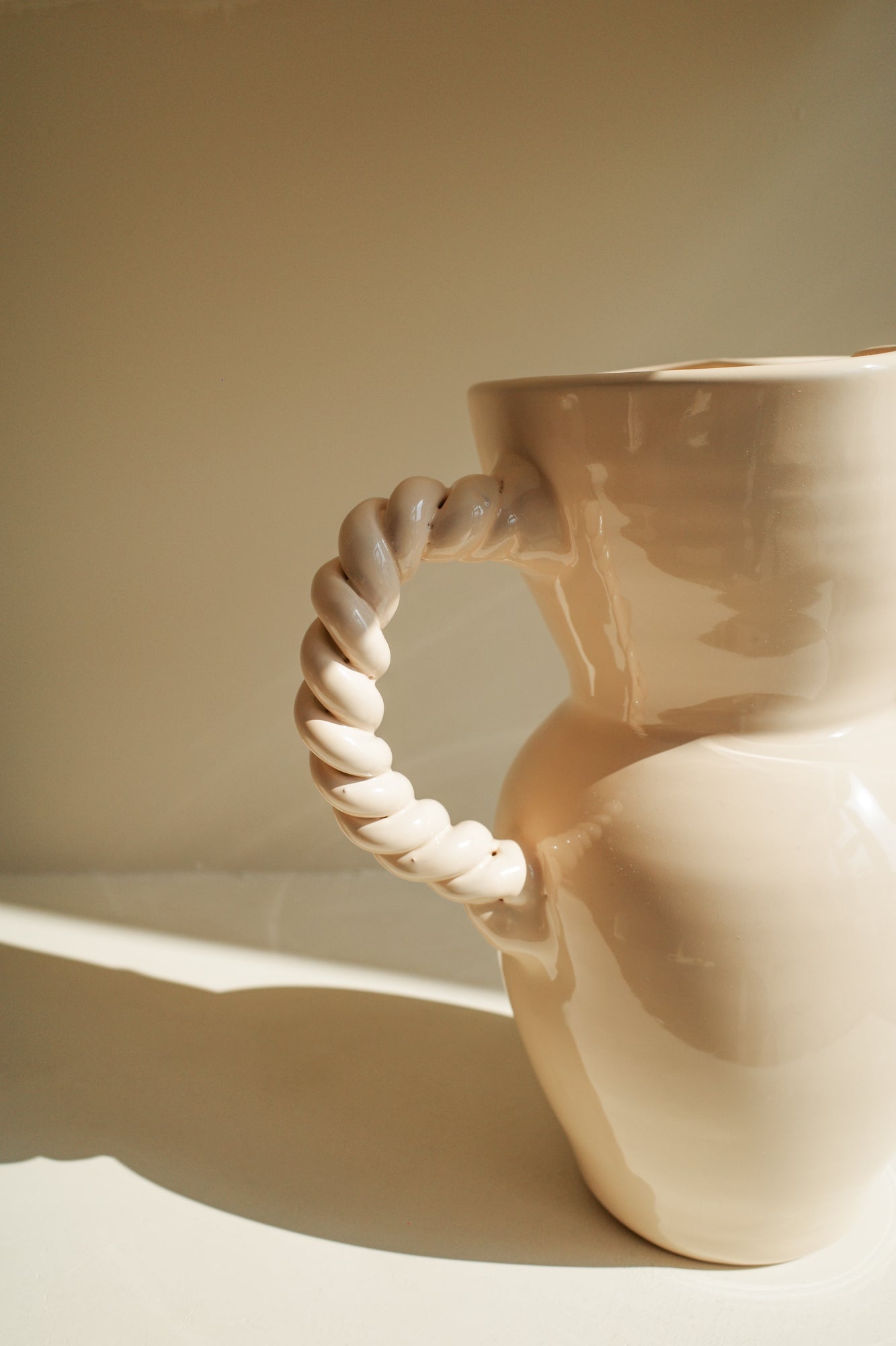 Cream glazed ceramic pitcher with pinched spout and braided handle.