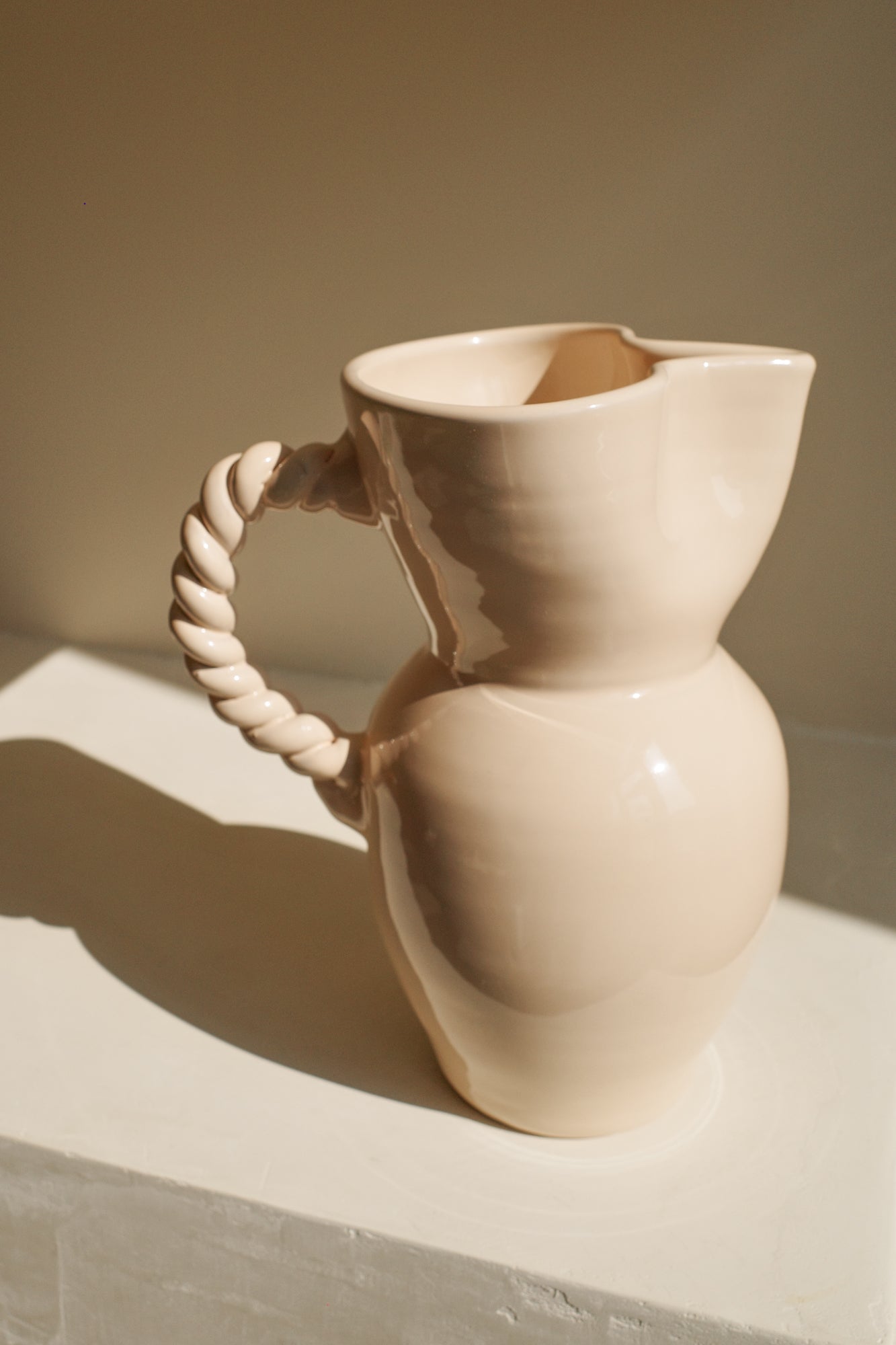 Cream glazed ceramic pitcher with pinched spout and braided handle.