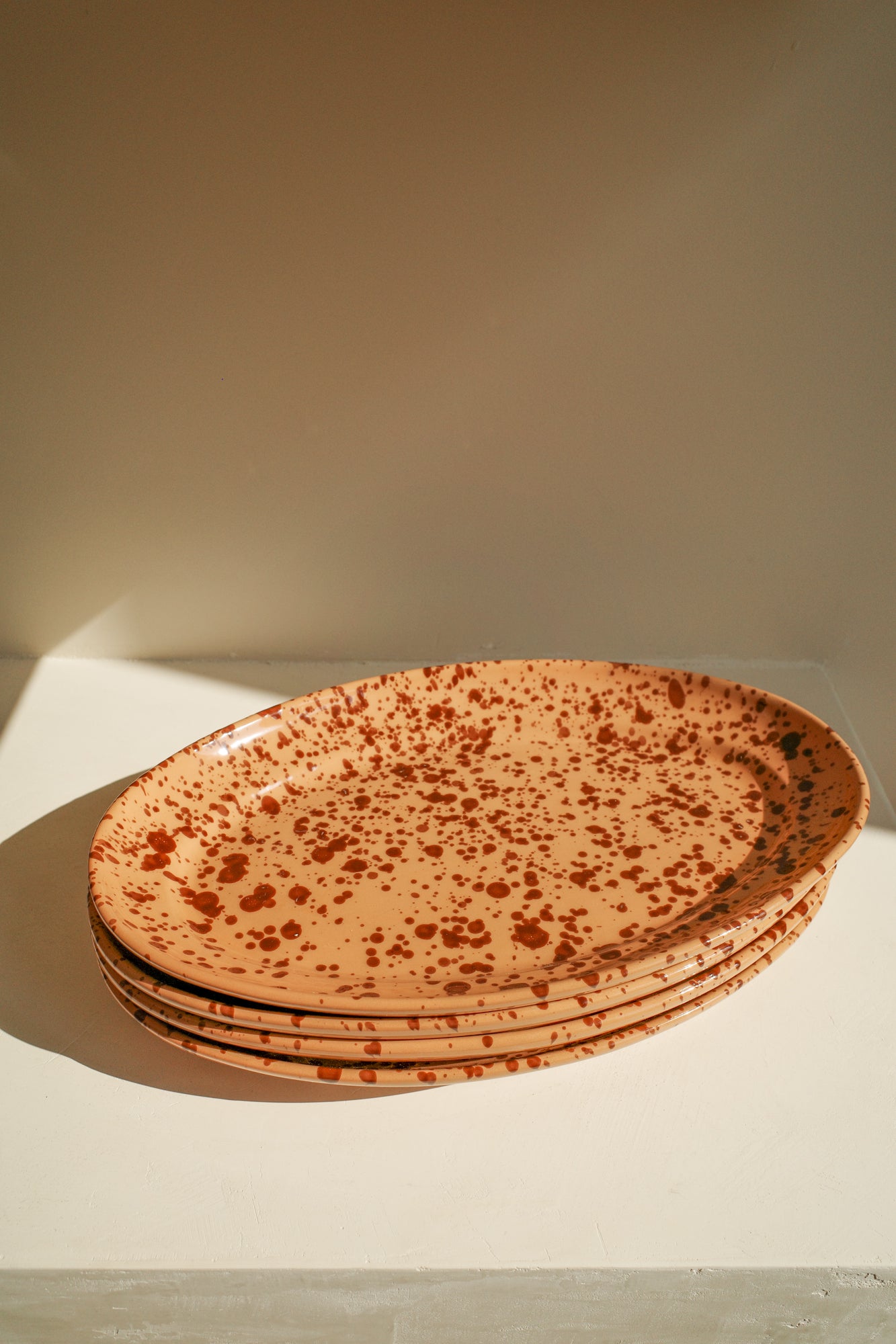 Stack of ceramic platters with terracotta glaze and dark brown paint splatter pattern.