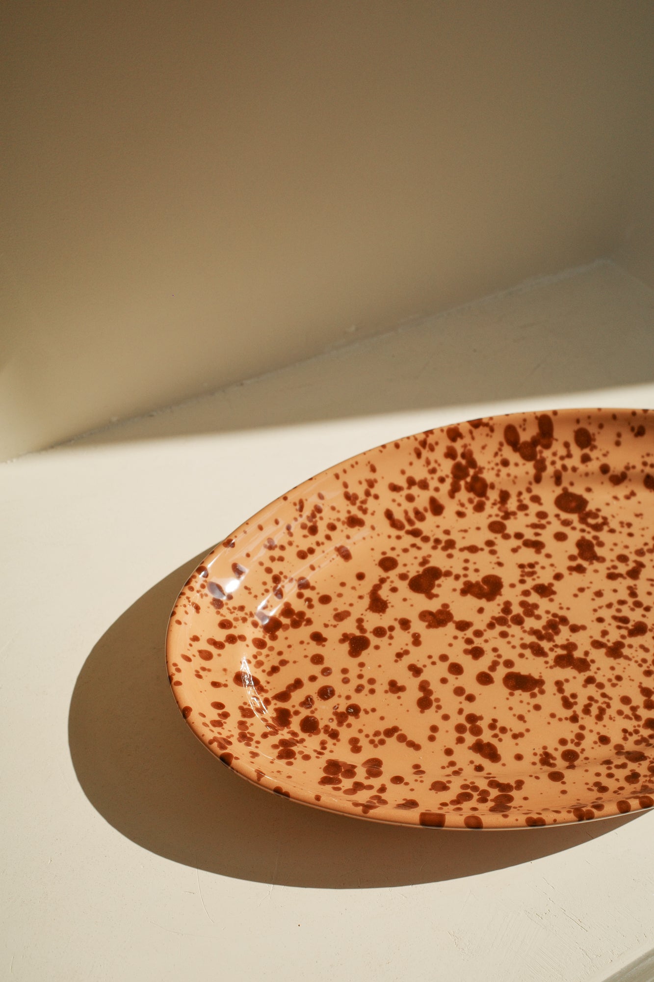 Ceramic platter with terracotta glaze and dark brown paint splatter pattern.