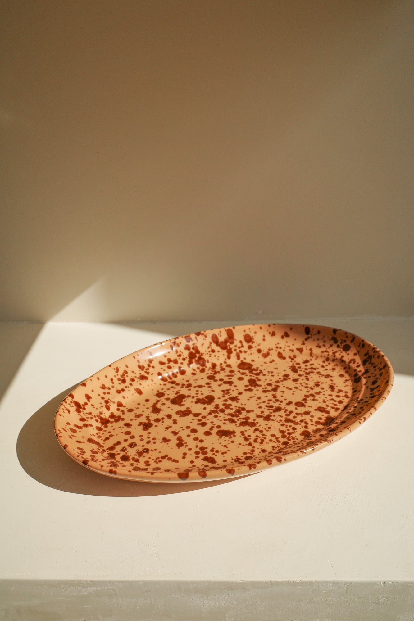 Ceramic platter with terracotta glaze and dark brown paint splatter pattern.