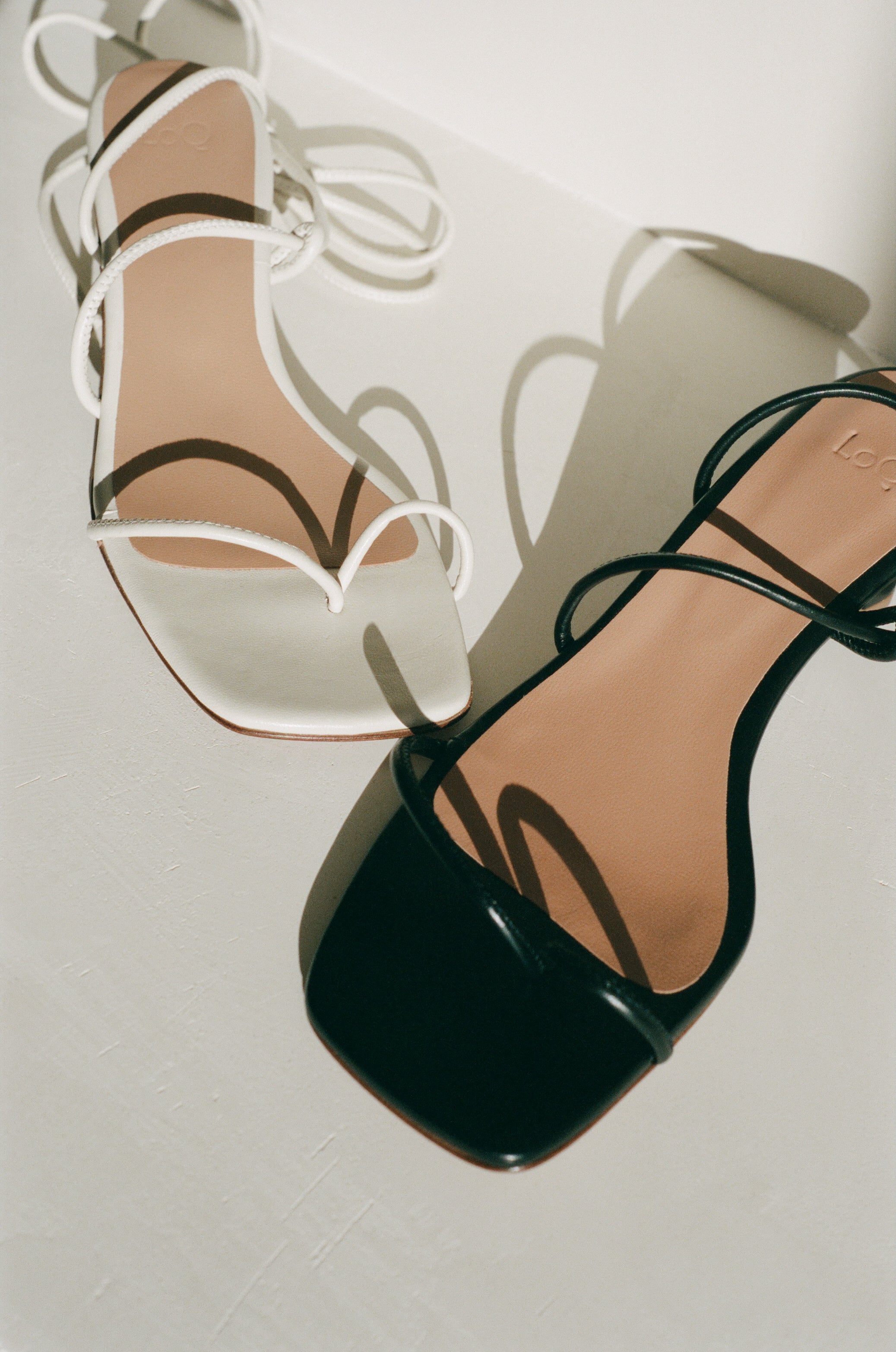 Heeled sandal in off-white leather featuring tubular leather straps that tie at the ankle and a small sculptural 2" heel; a minimal strap divides at the toe.