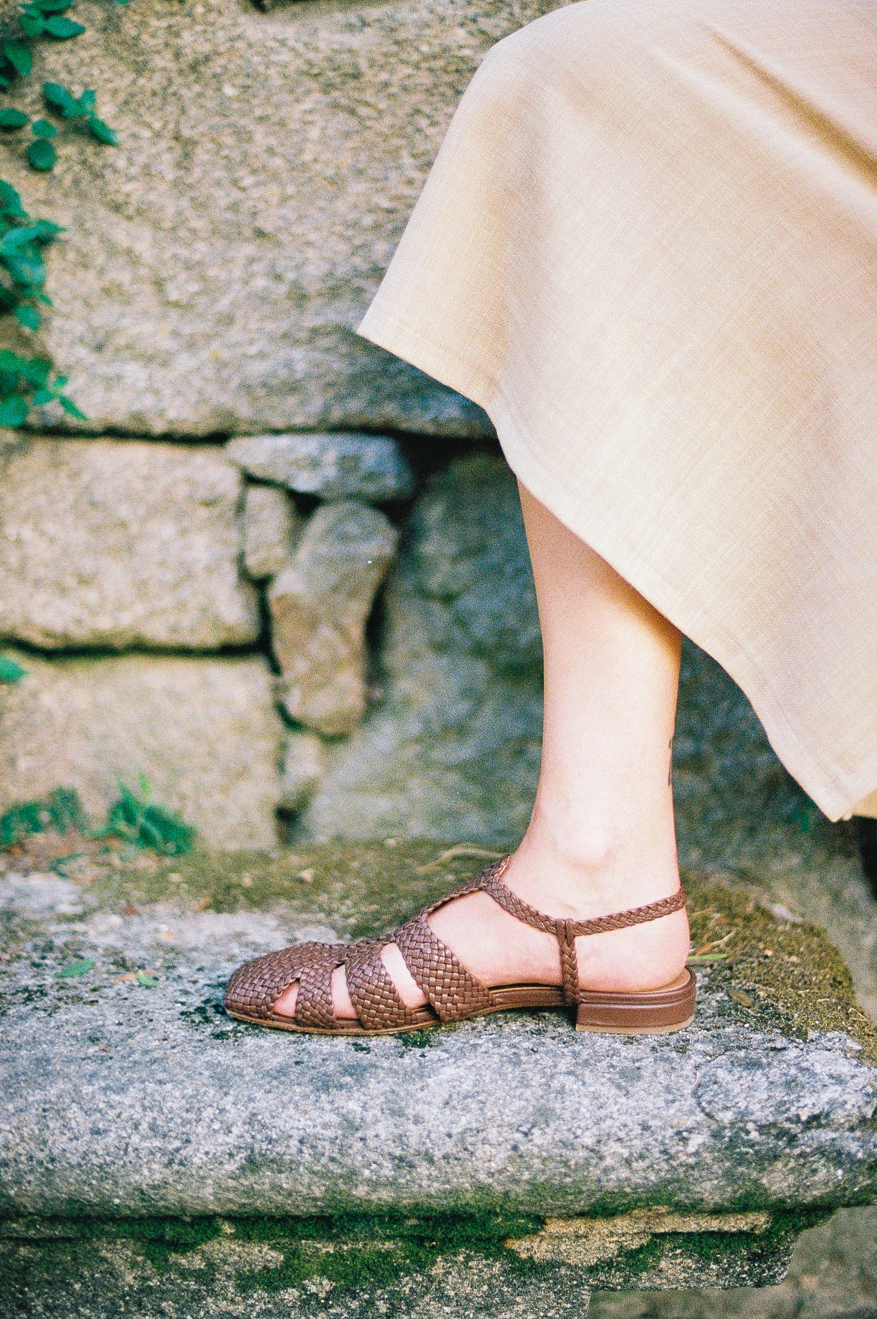 Brown leather fisherman-style sandals featuring straps made of woven leather across the foot and a strap that buckles around the ankle